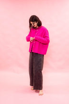Person wearing a neon pink hand knitted cashmere oversized cardigan and dark pants against a pink background

