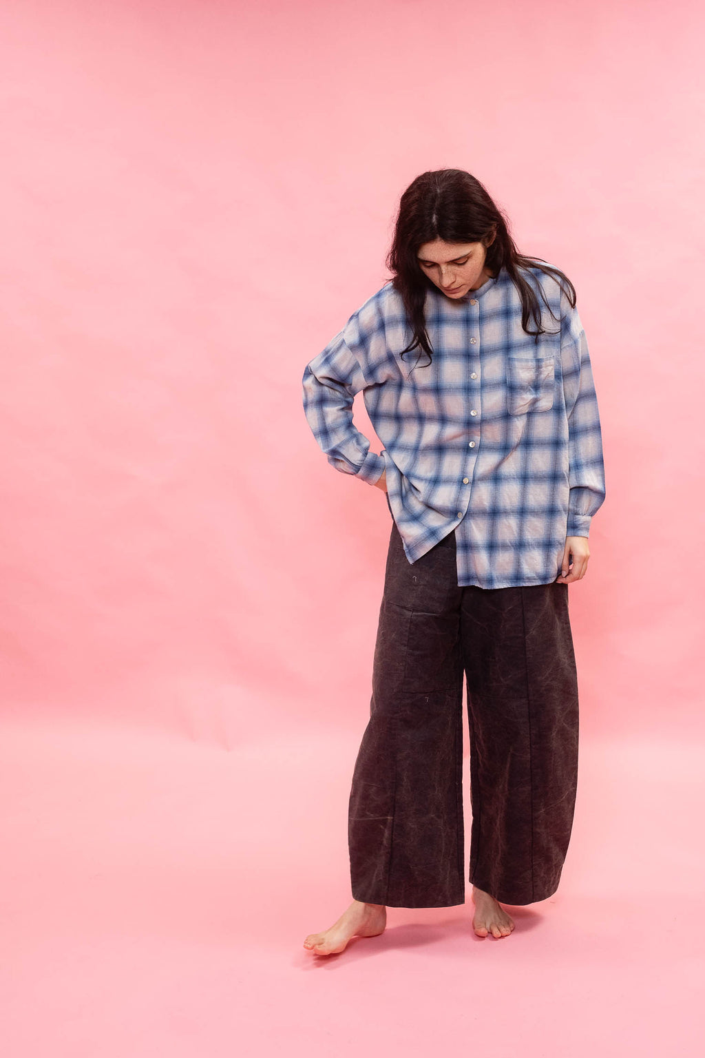 Person wearing a blue plaid cotton wool brushed Japanese cotton shirt and dark pants on a pink background
