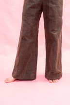 Brown wide-leg cotton
 pants shown on a model from the waist down, standing barefoot against a solid pink background.