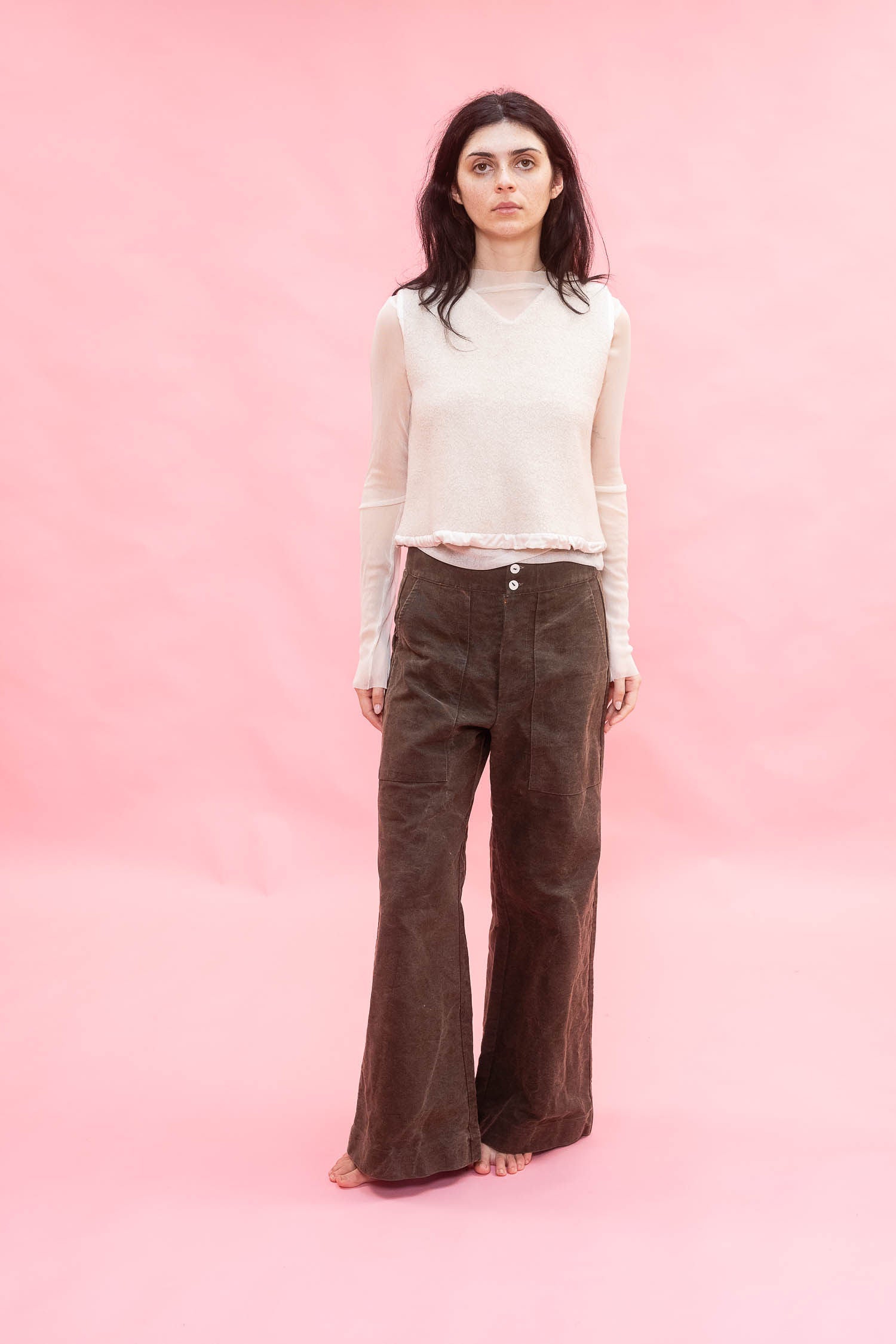 Woman wearing a white top and brown cotton wide leg 
pants against a pink background