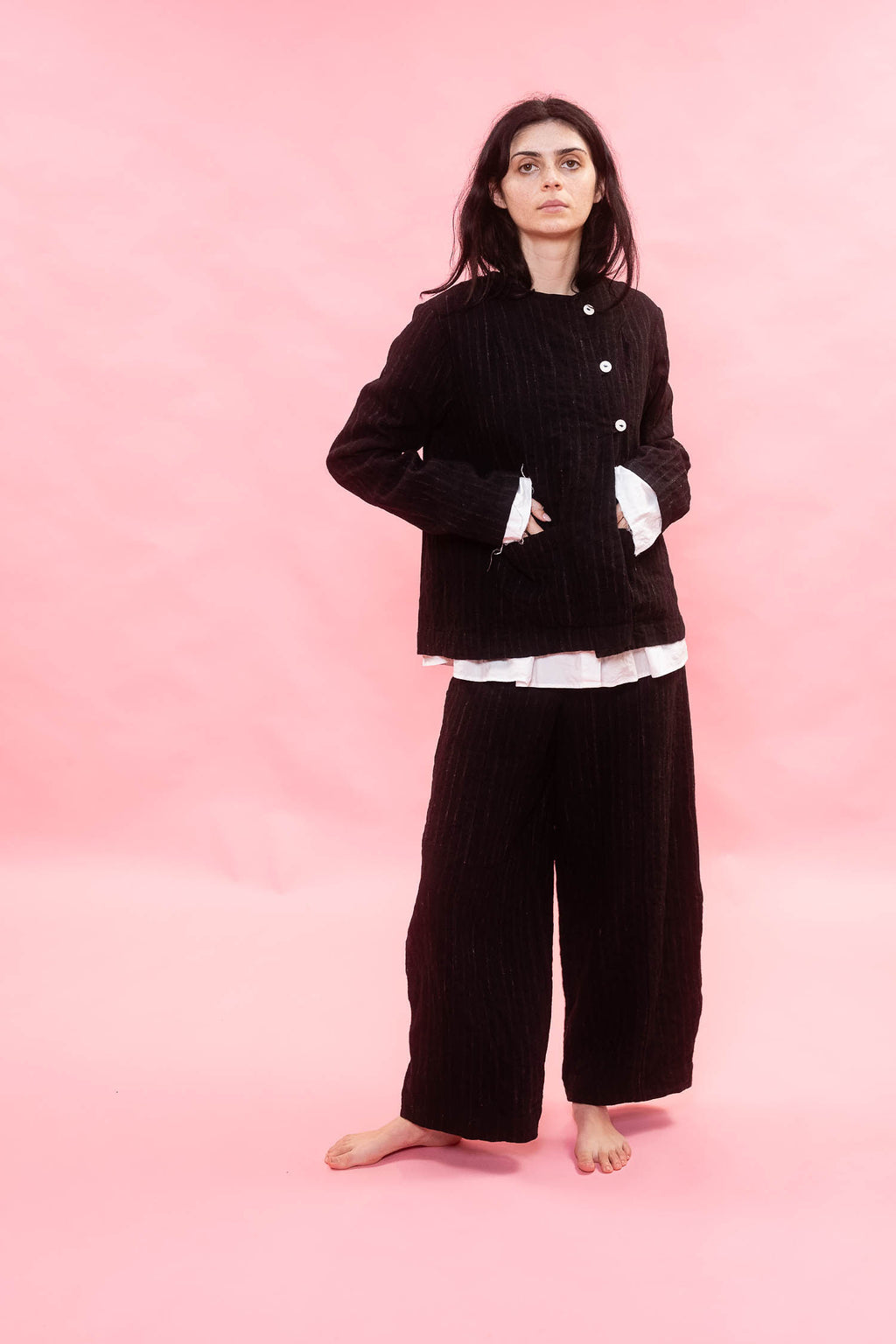 Person wearing a black wool pinstripe jacket with white buttons on a pink background