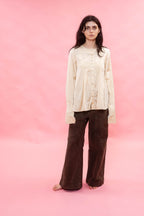 Woman wearing a cream pin tuck pleated silk cotton satin blouse and brown pants on a pink background