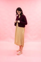 Woman wearing a plum fluffy alpaca knit cardigan over a beige dress on a pink background
