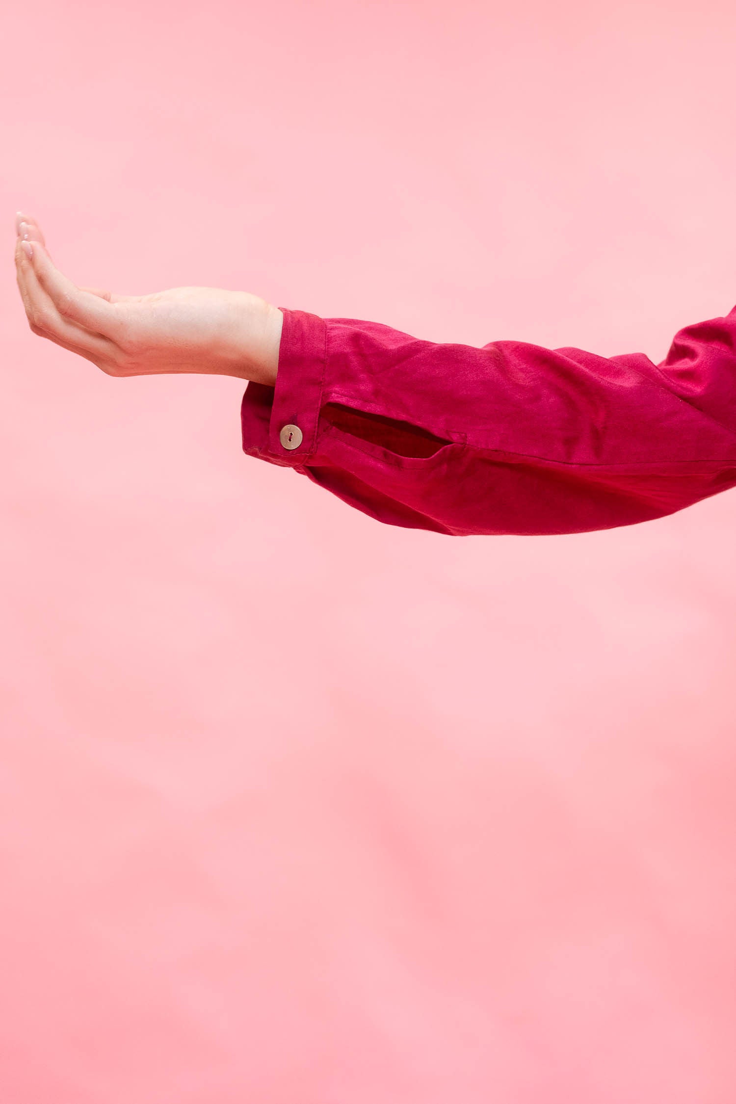 A person's outstretched hand and forearm wearing a bright pink long-sleeve top against a solid pink background.