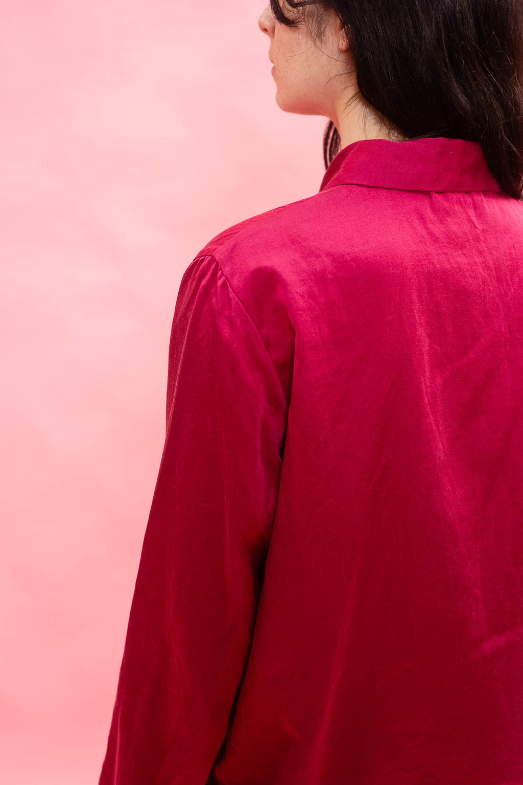 A close-up back view of a person wearing a bright magenta pink satin button-up shirt against a solid pink background.