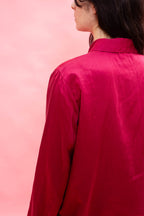 A close-up back view of a person wearing a bright magenta pink satin button-up shirt against a solid pink background.