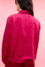 A person shown from the back wearing a bright magenta pink long-sleeve button-up shirt against a solid pink background.
