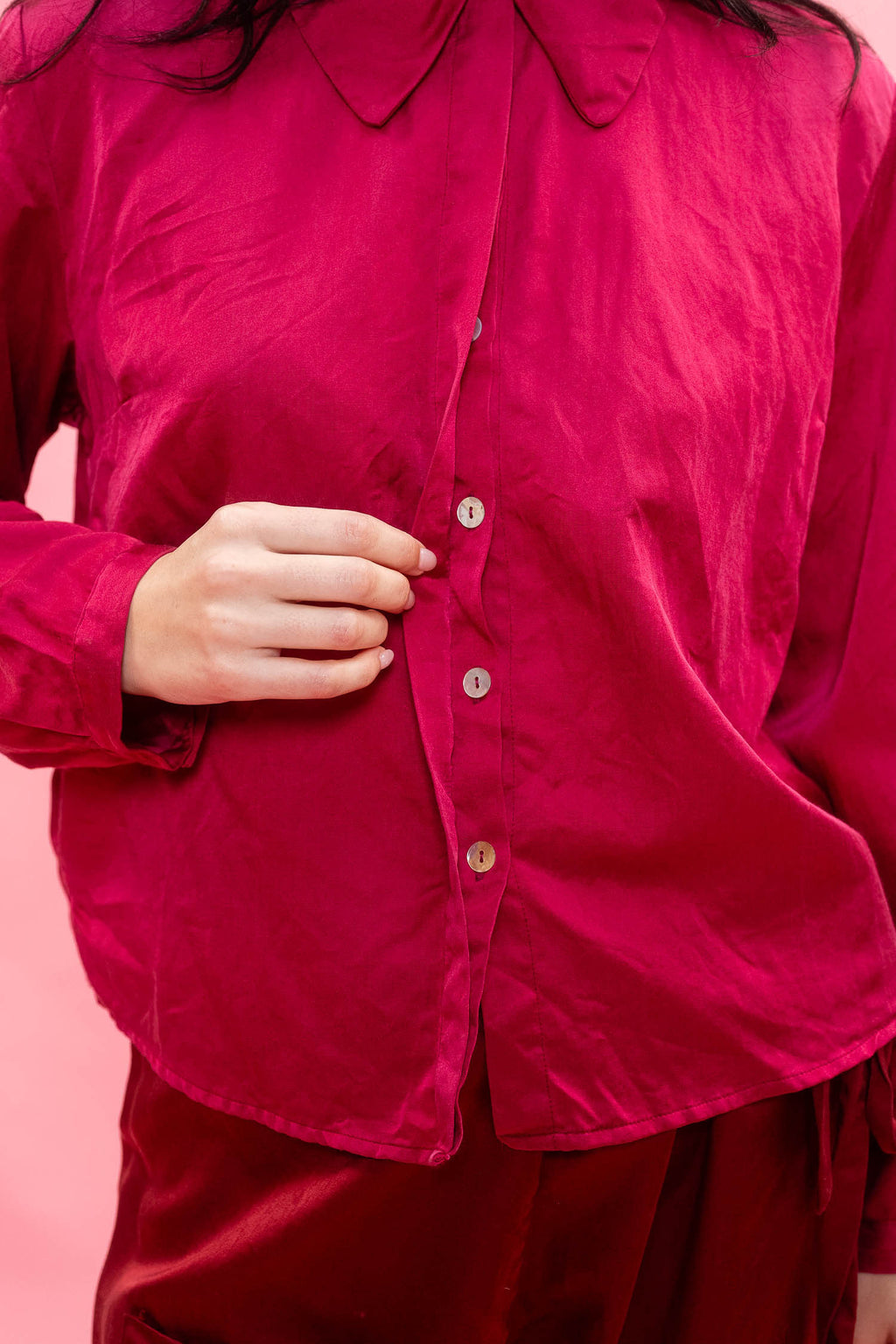 A close-up of a person wearing a bright magenta button-up shirt and matching pants, with one hand adjusting the front buttons.