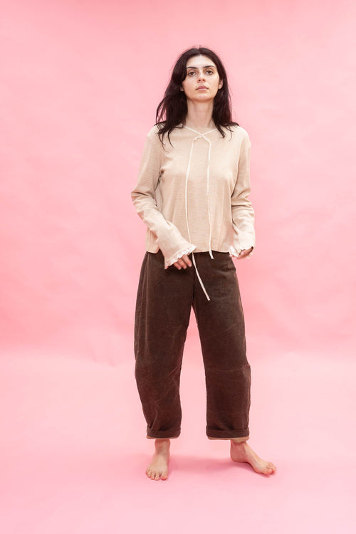 Woman wearing a beige shirt and dirt green brown pants on a pink background
